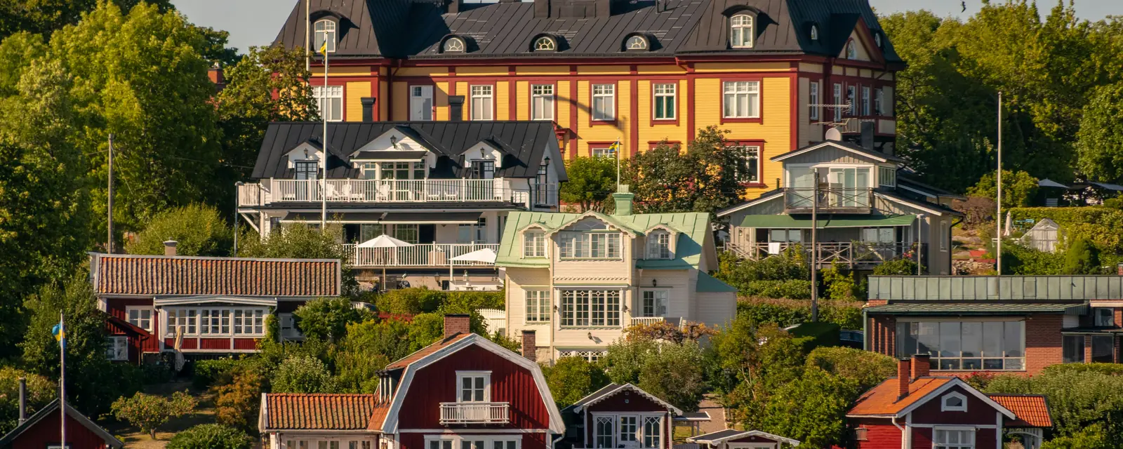 Svenskt skärgårdssamhälle med röda stugor och en gul herrgård vid vattnet